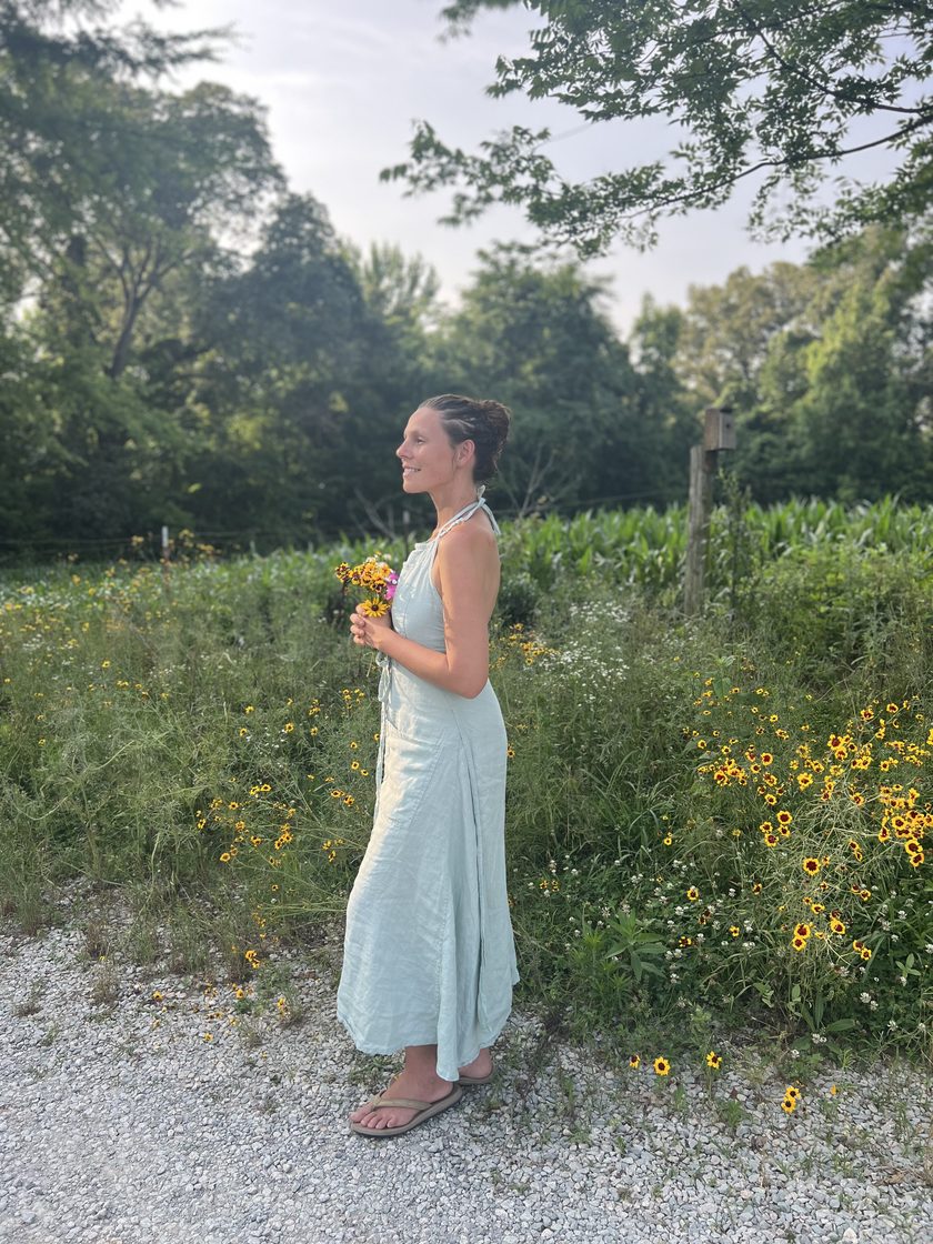 Katt in a white dress in a summer meadow, holding a bunch of wildflowers